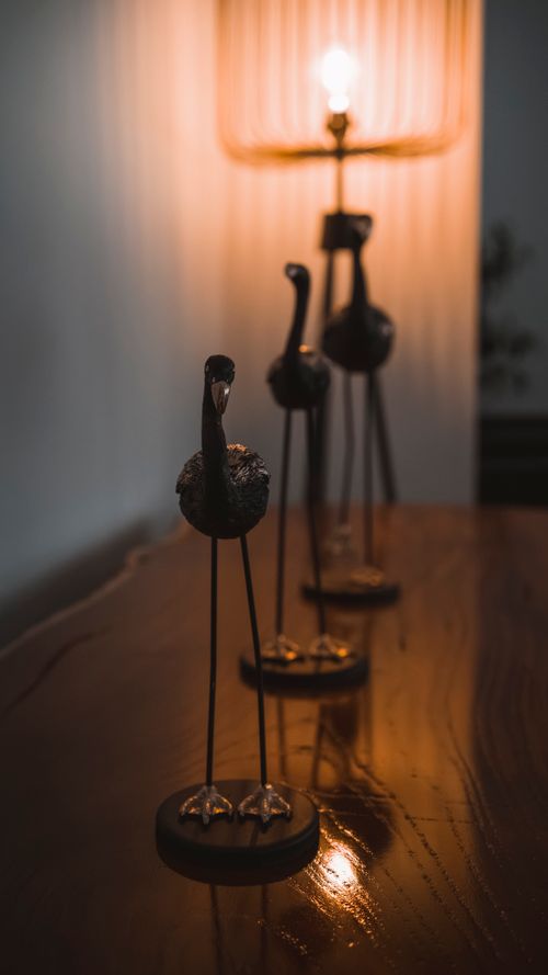 Free Antique bird sculptures with warm candlelight ambiance on a wooden table, capturing elegance and tranquility. Stock Photo