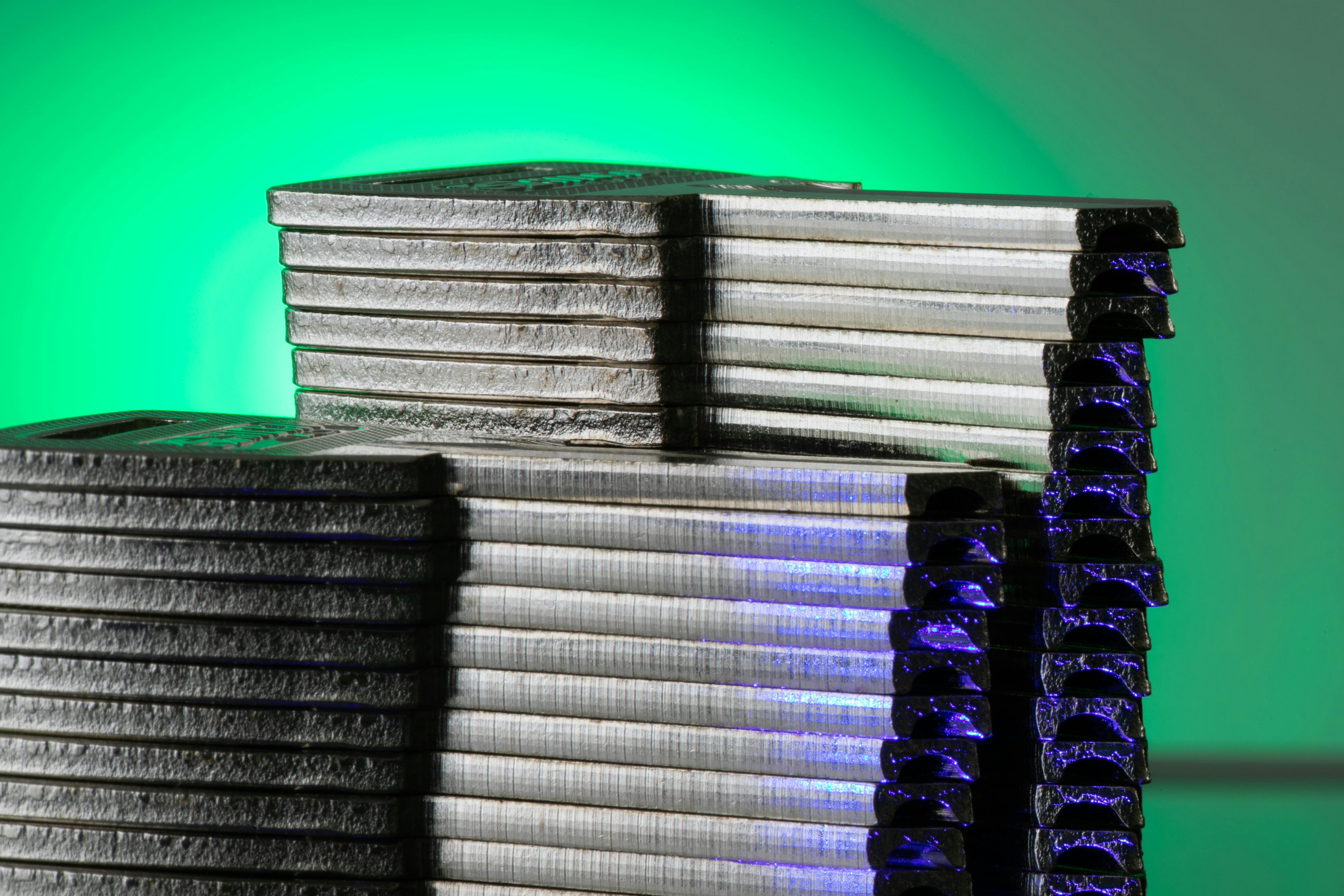 Close-up of stacked metallic discs reflecting green and blue light.