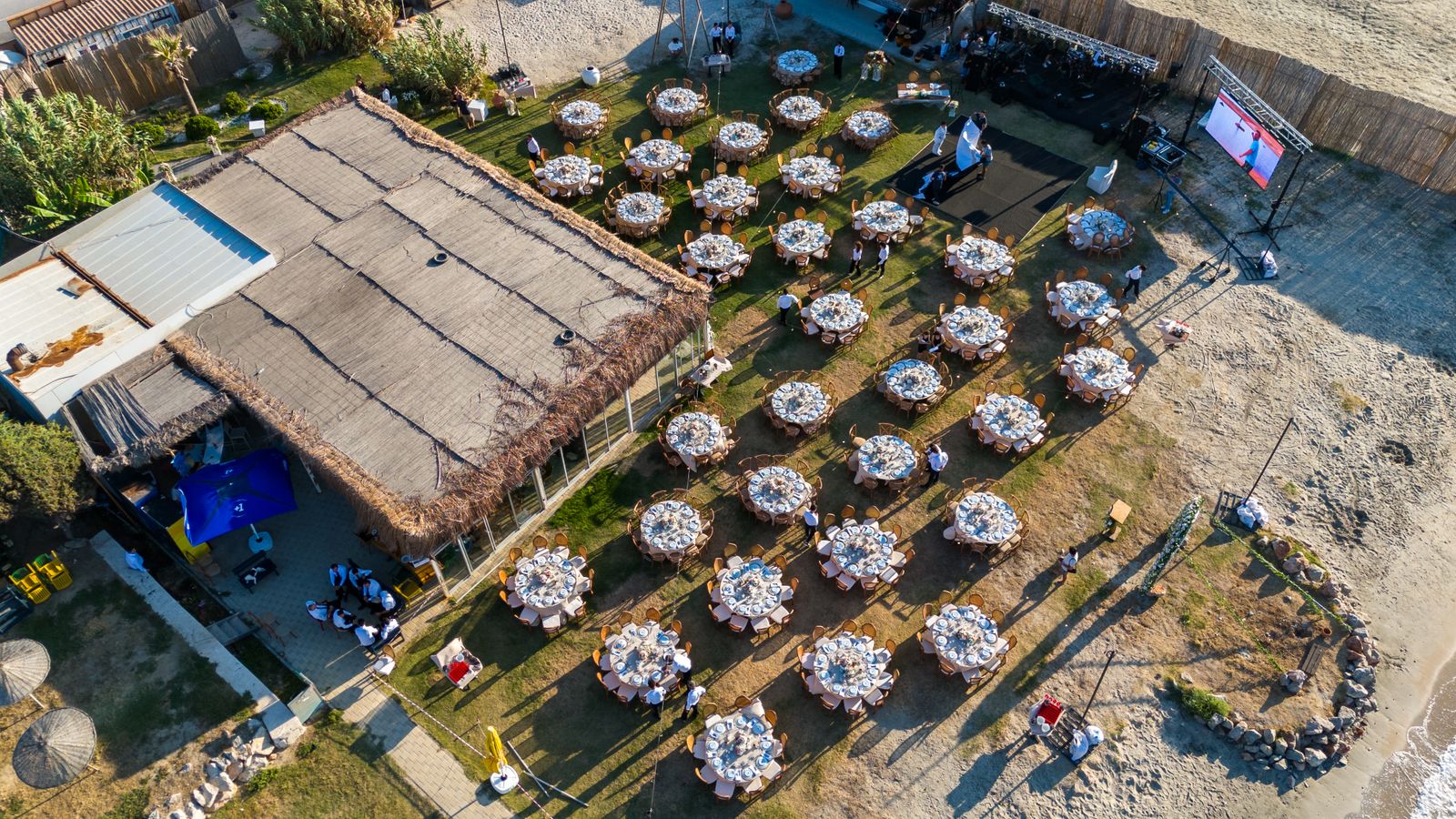 Aerial view of a beach reception with tables and warm lighting.