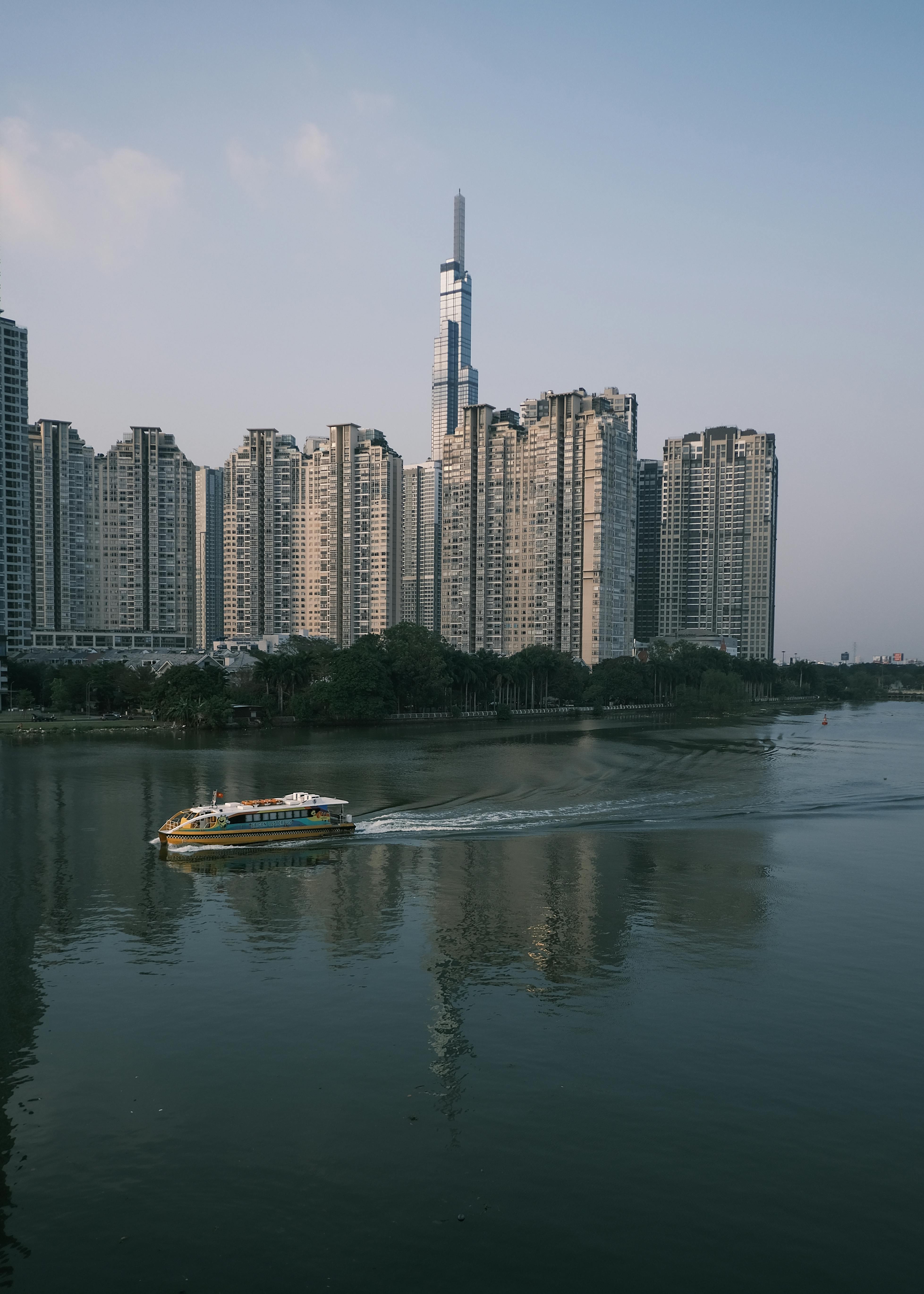 Scenic view of a modern skyline with tall buildings and a river in Ho Chi Minh City, featuring a watercraft.