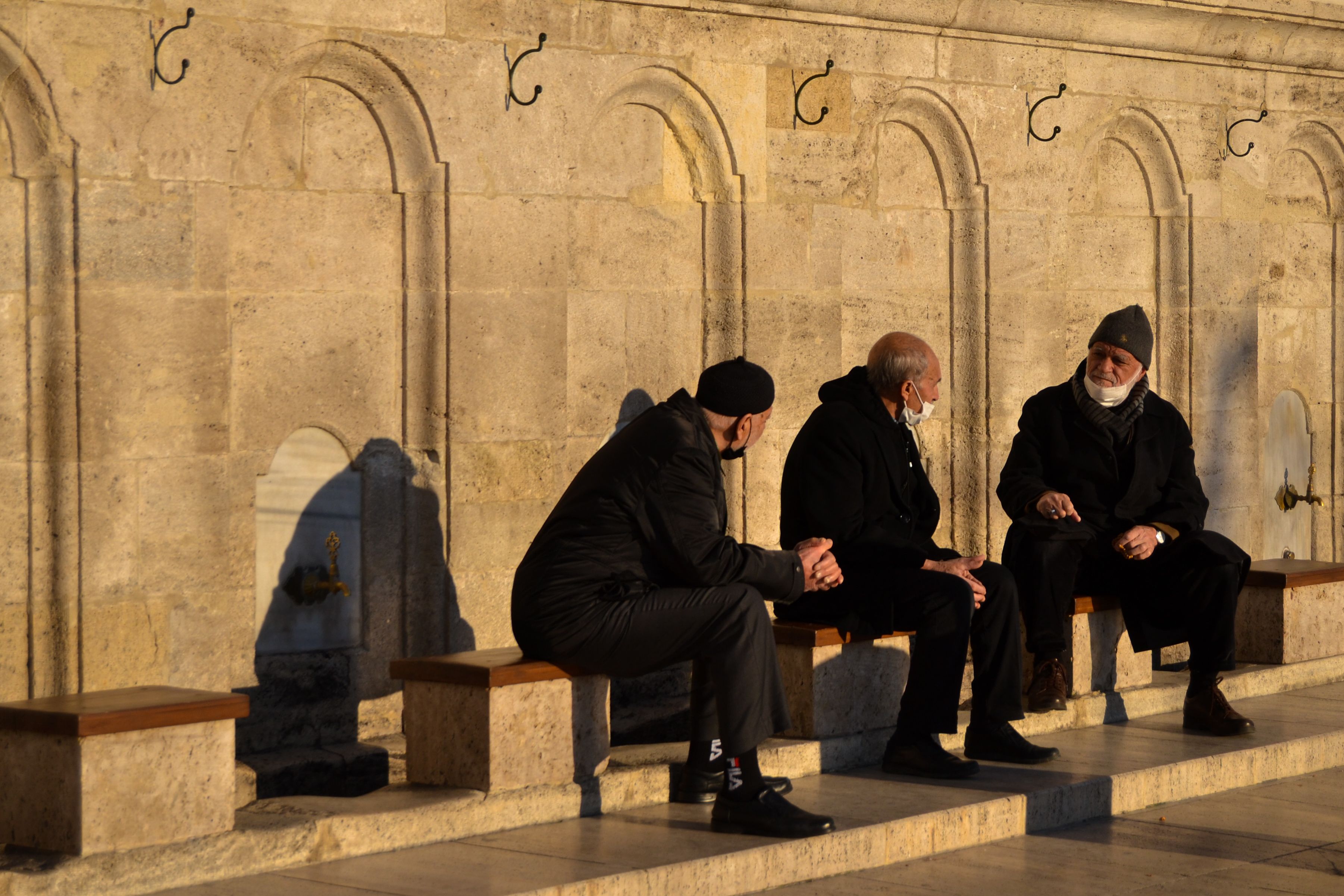 Three men sitting on benches in front of a wall · Free Stock Photo