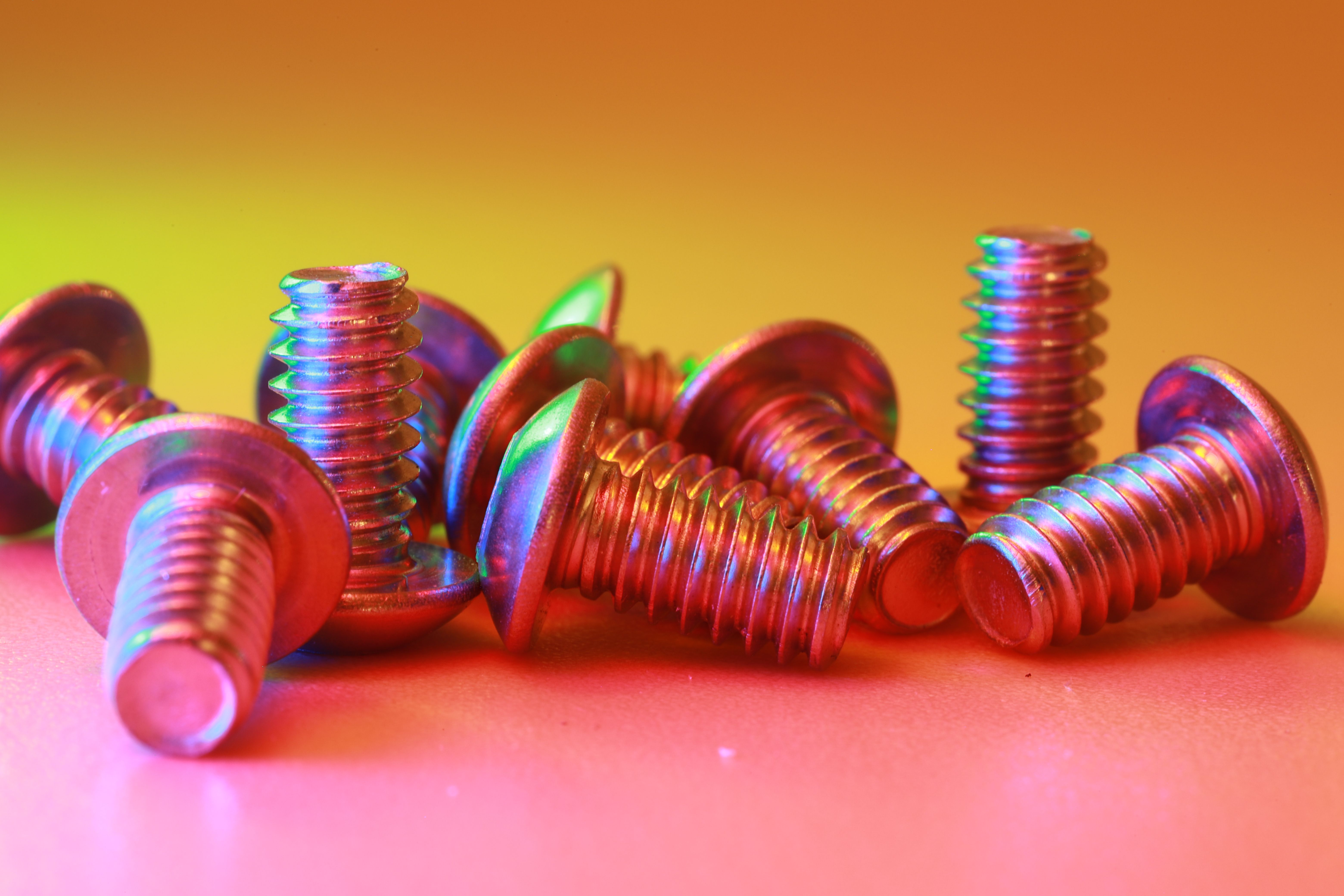 Vibrant image of metallic screws with rainbow reflections on an orange gradient backdrop.