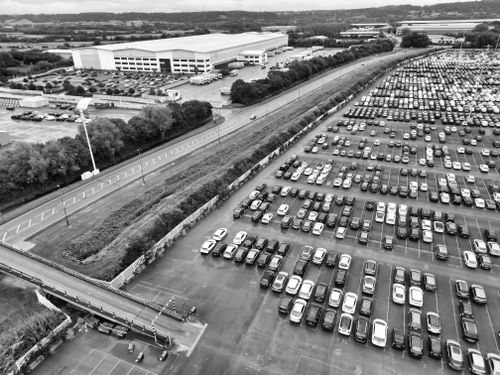 Free Aerial perspective of a large car park beside an industrial warehouse in England. Stock Photo