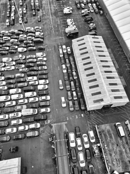 Free Black and white aerial shot of a crowded parking lot in England, featuring cars and a warehouse. Stock Photo