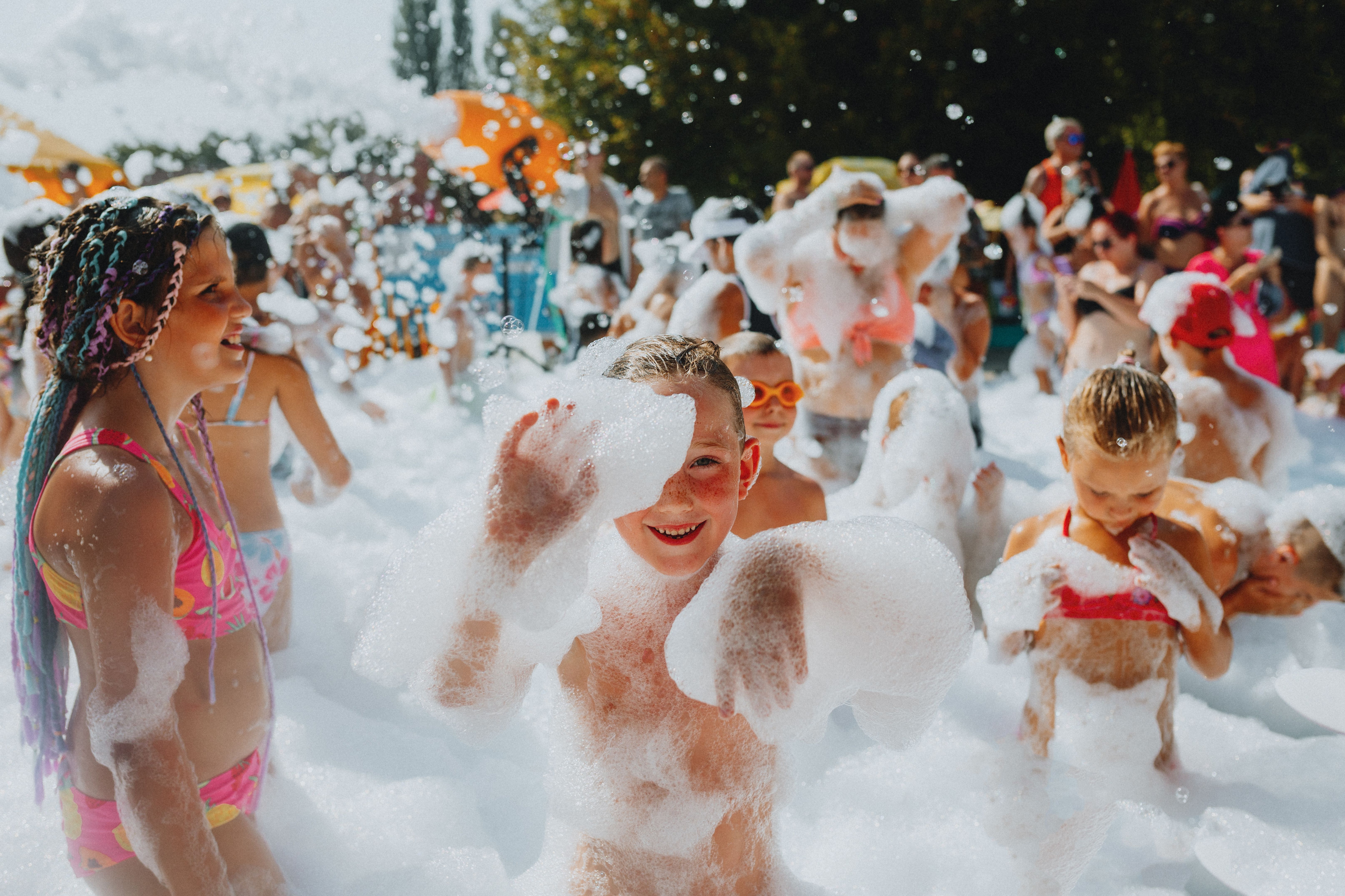 Children playing in a foam-filled outdoor water party, smiling and splashing in the sun