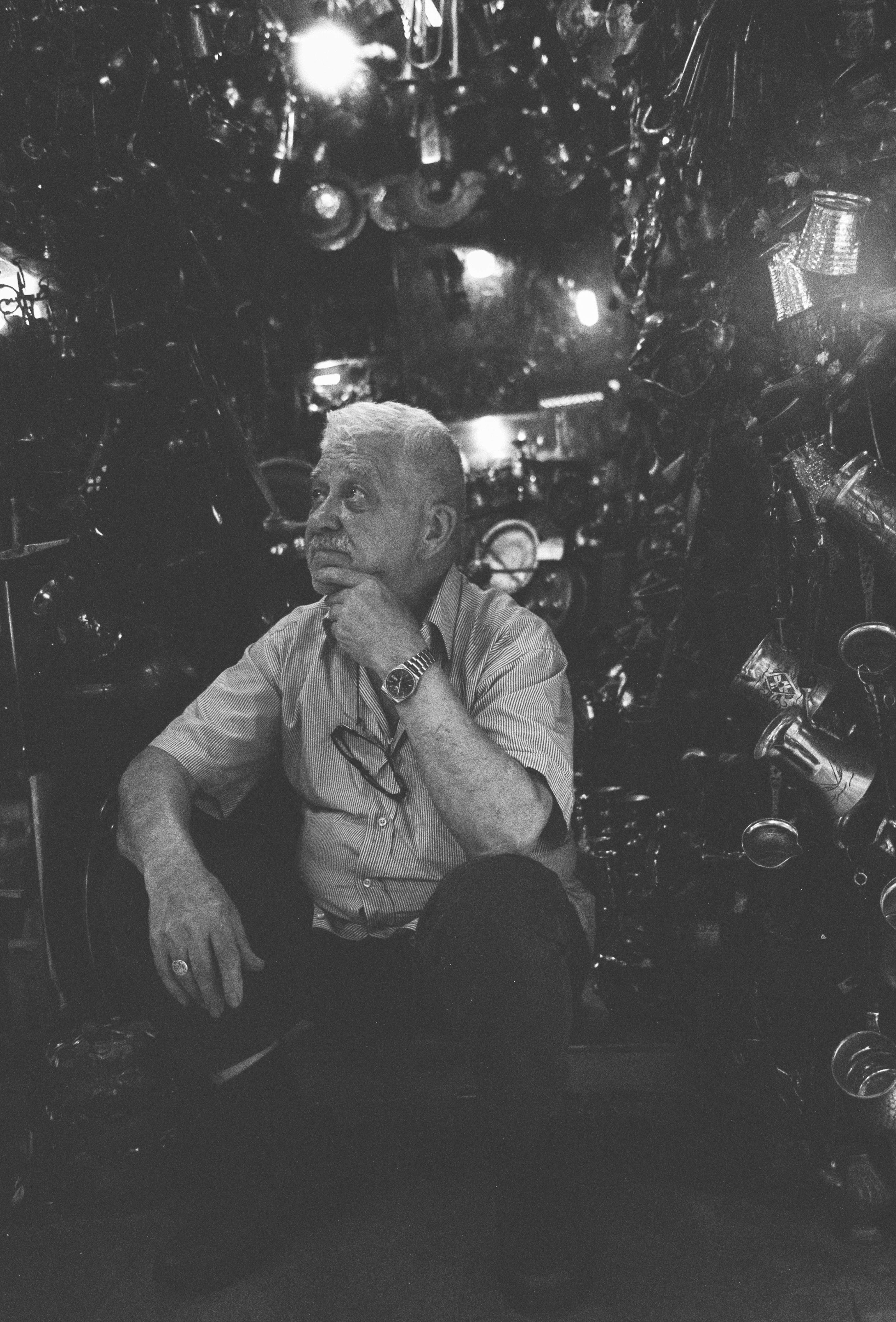 Elderly man surrounded by eclectic gadgets in Istanbul, capturing a moment of reflection.