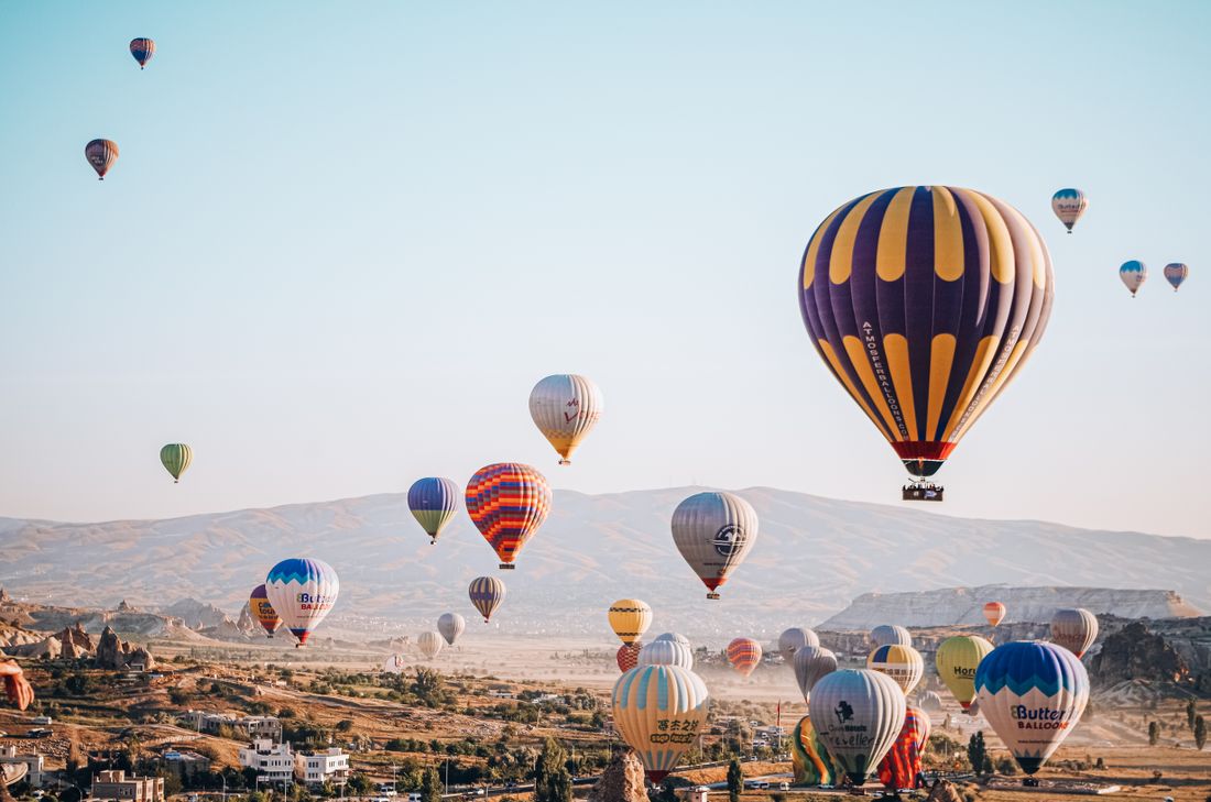 Many hot air balloons flying over palms and sugarcane at dawn near Luxor