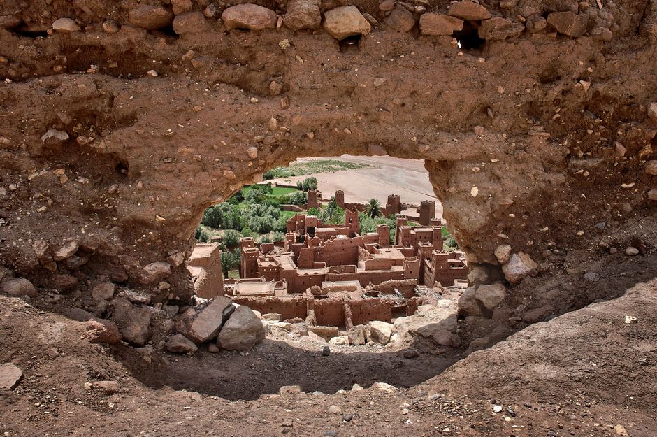 View of a historic village through a natural rocky archway in a desert landscape.