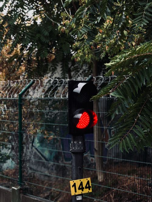 Free Red traffic light against a fence and foliage background capturing urban atmosphere. Stock Photo