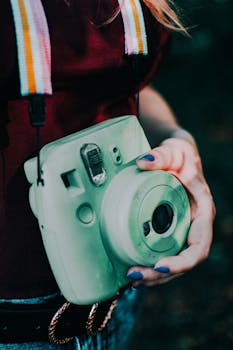 A person holding a mint green instant camera with colorful strap, showcasing retro style.