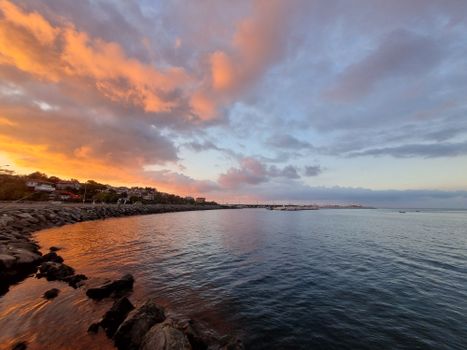 Beautiful sunset over a rocky shoreline with vibrant skies and tranquil waters.
