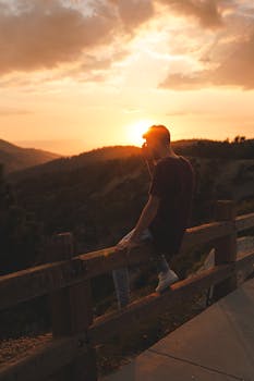 一名男子坐在木栅栏上，在美丽的日落背景下享受平静的时刻