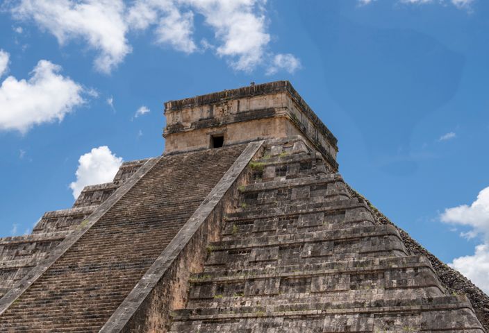 Explore the iconic stepped pyramid of Chichén Itzá against a bright blue sky.