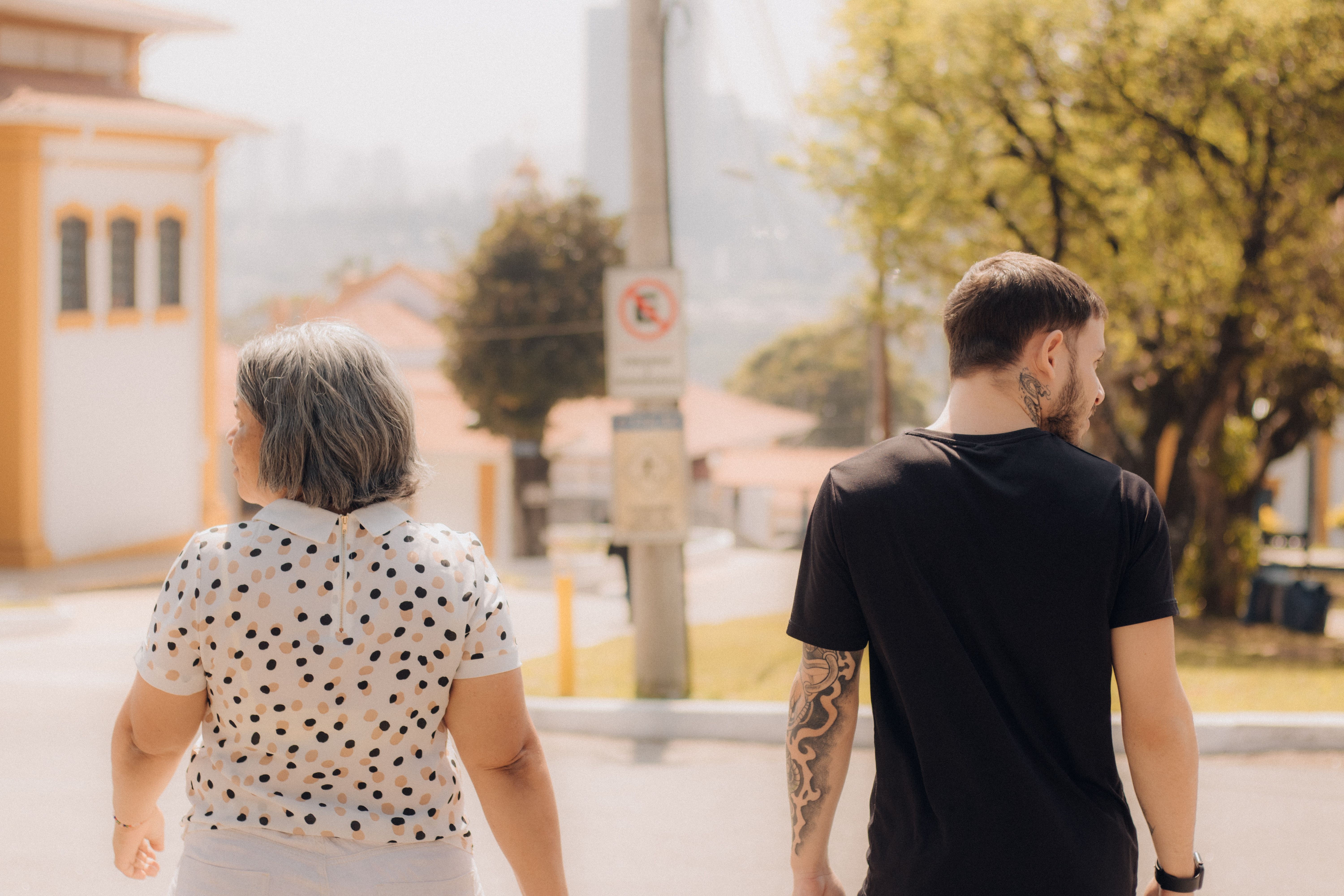 A man and a woman walk down a sunny street, viewed from behind. Casual, outdoor scene.