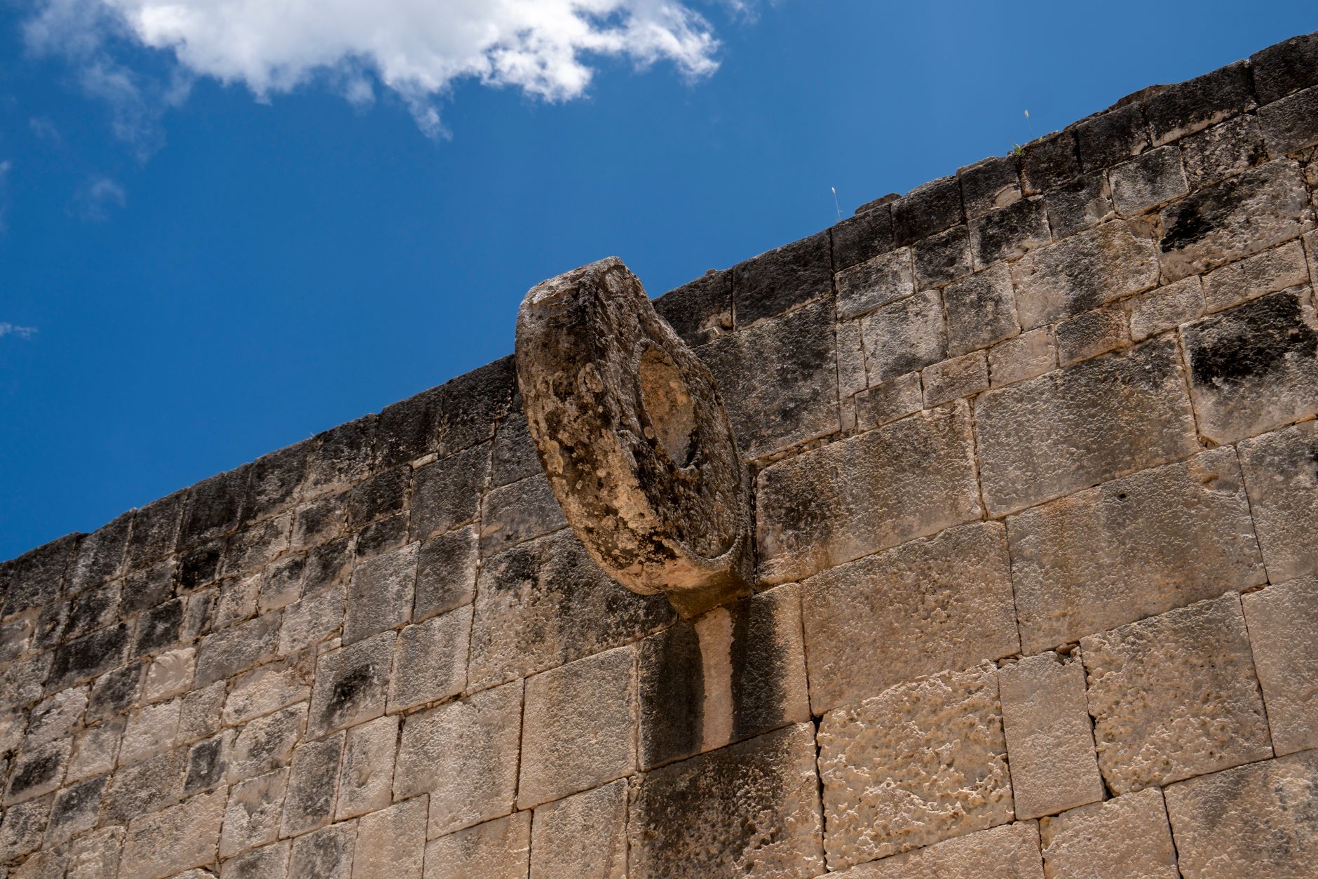 Close-up of a Mayan ball game ring on a stone wall in Chichén Itzá, under a clear blue sky.