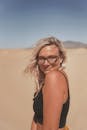 一位金发女子戴着眼镜，在沙漠中摆出姿势，展示夏季时尚