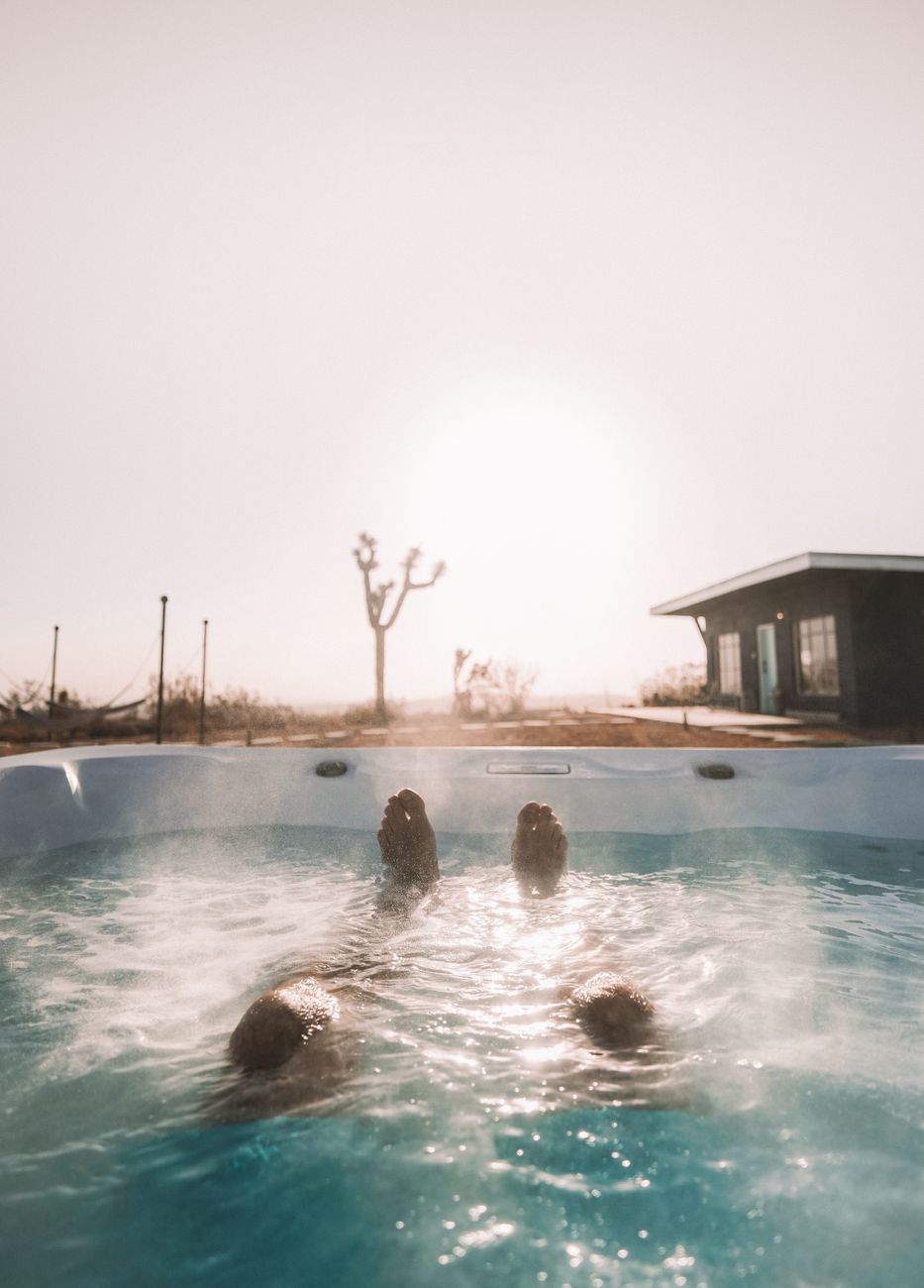Person enjoying a steamy hot tub with desert landscape at sunrise in Joshua Tree, California.