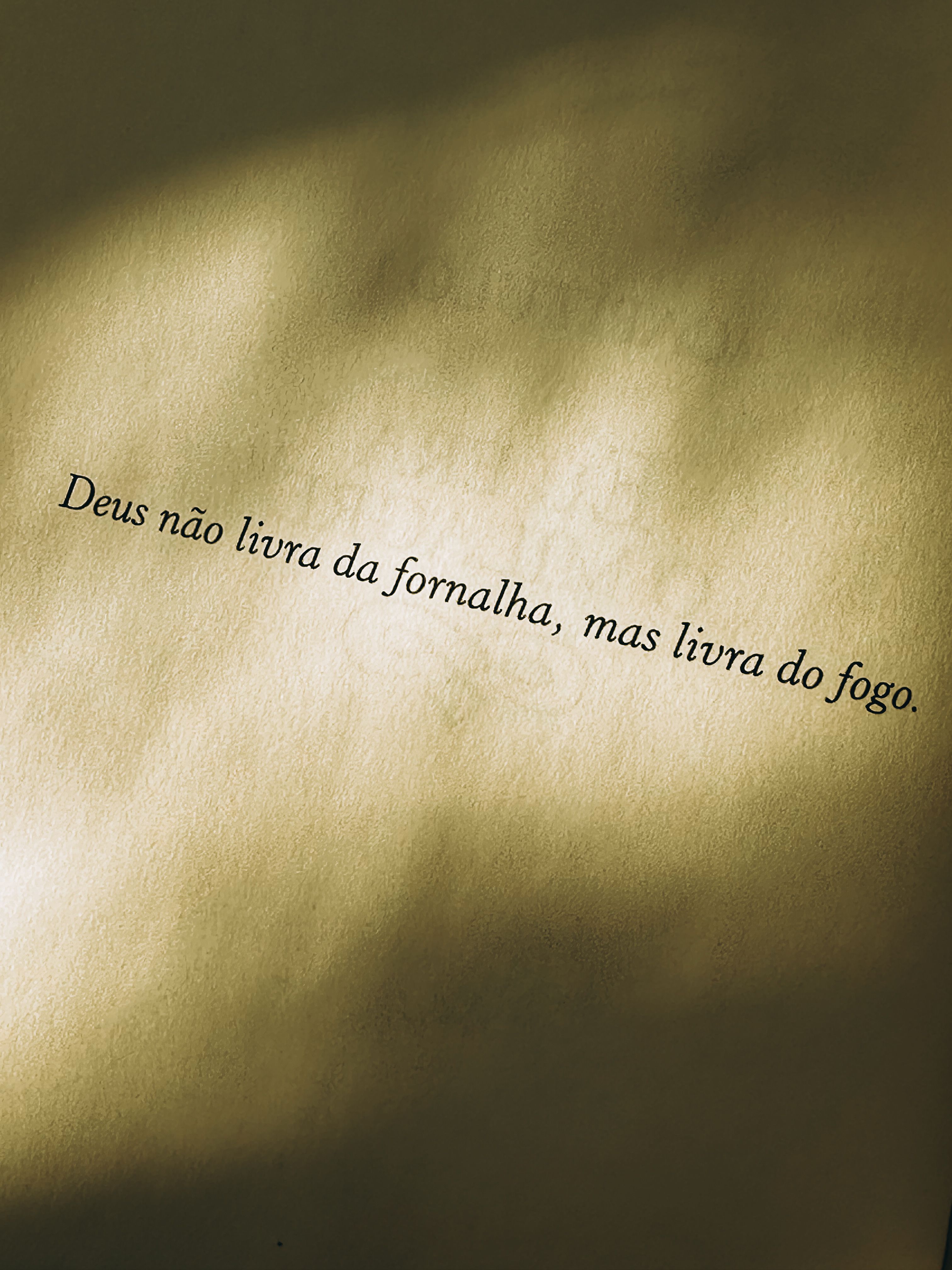 Quote 'Deus não livra da fornalha, mas livra do fogo' on textured paper with light shadows.