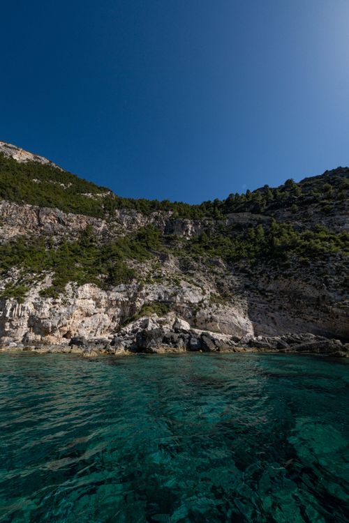 Free Rocky cliff with lush greenery above clear turquoise sea under blue sky. Stock Photo