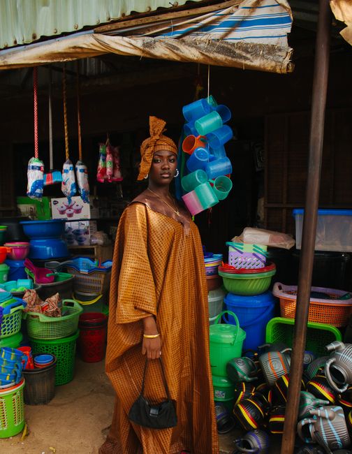 A woman in traditional African attire stands amidst colorful market goods, showcasing vibrant culture.