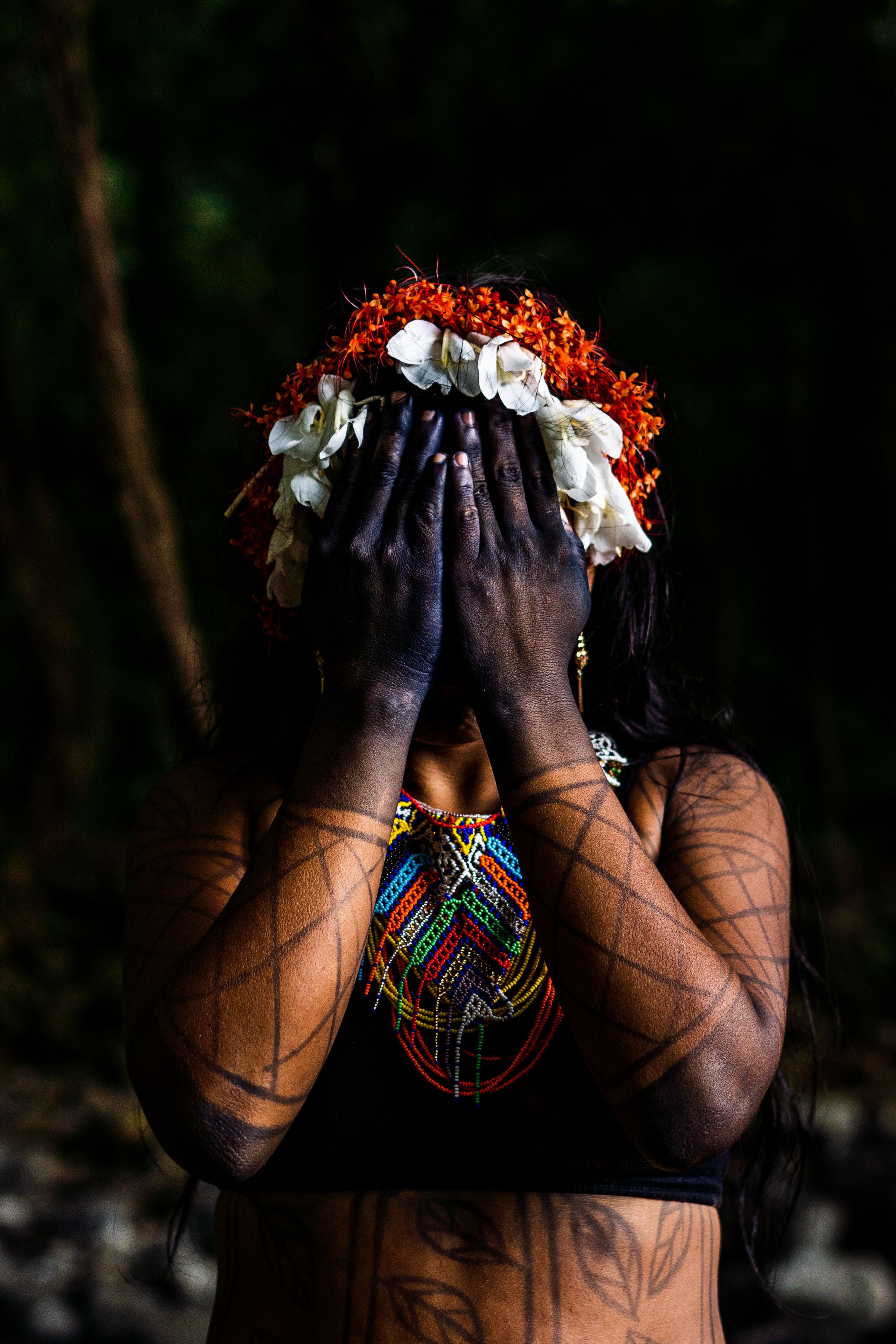 Portrait of an indigenous woman with tribal art, wearing flowers in a forest setting.