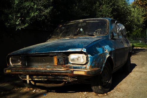 Free A rusty, classic car sits abandoned on a sunny street, showcasing nostalgic decay. Stock Photo