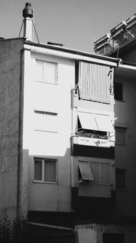 Black and white photo of an urban apartment building facade with windows and balcony shades.
