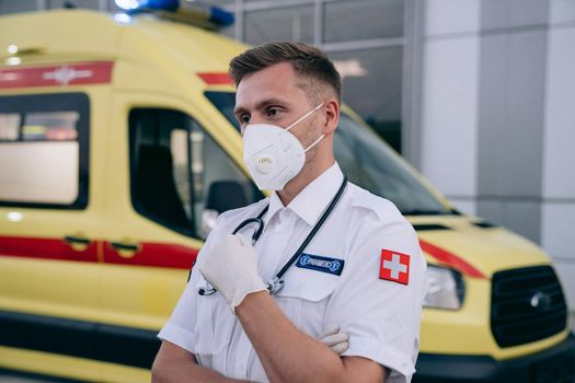 Paramedic wearing a mask and stethoscope standing confidently in front of an ambulance.