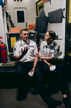 Two paramedics in uniform sit in an ambulance discussing their work, fostering teamwork.