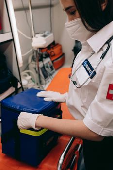 A female paramedic in uniform preparing medical equipment inside an ambulance.