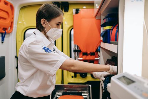 Free A female paramedic wearing a mask organizes supplies inside an ambulance, focusing on readiness. Stock Photo