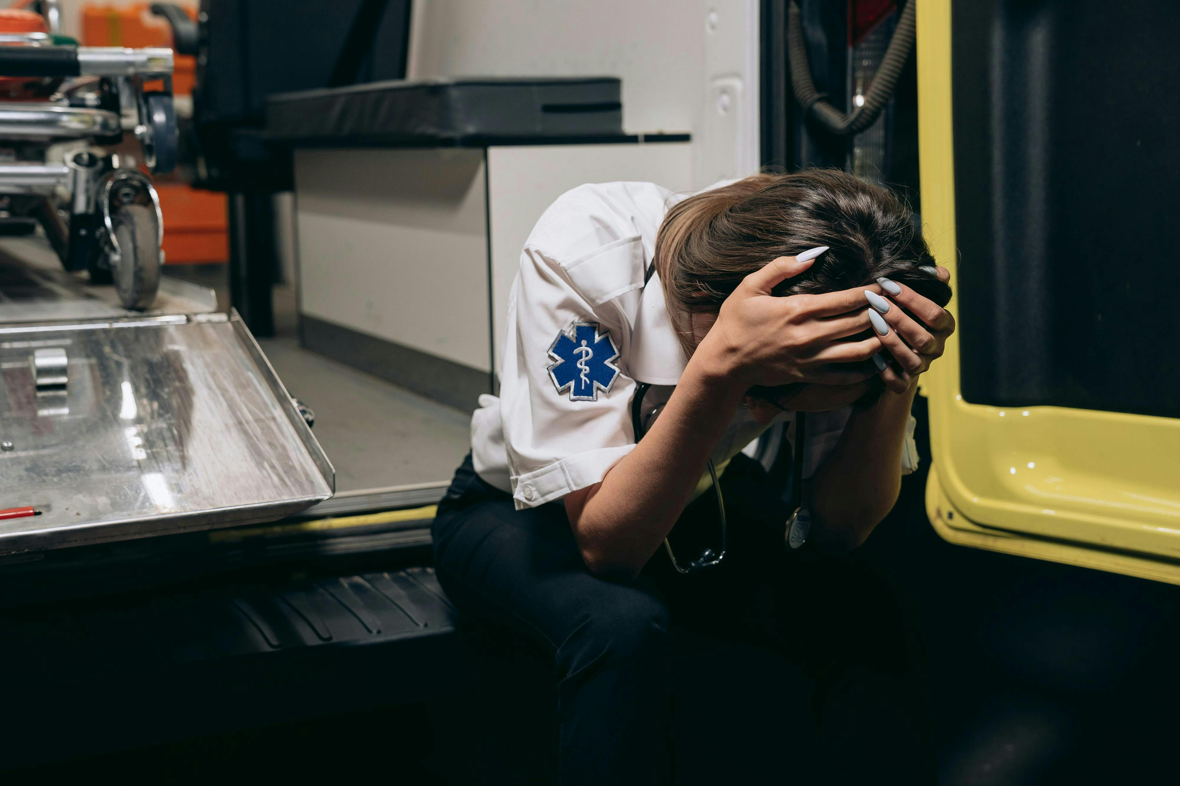 distraught paramedic sitting with her head in hands on the bumper of an ambulance