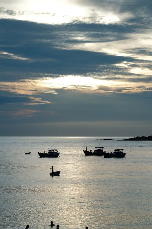 Free Tranquil sunset over the ocean with silhouetted boats and fishermen in an idyllic setting. Stock Photo