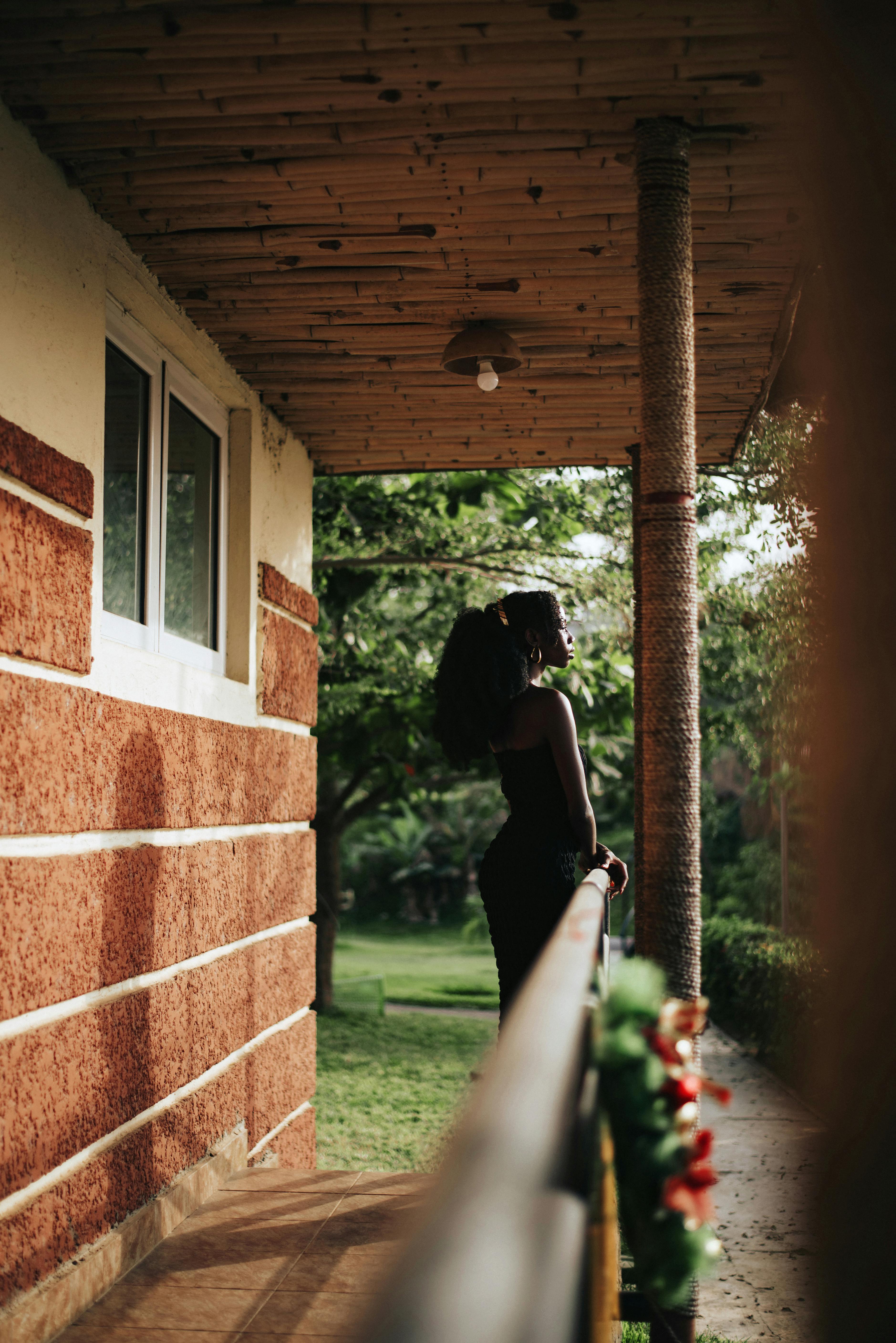 A woman stands elegantly on a balcony, enjoying a tranquil summer day in Abuja, Nigeria.