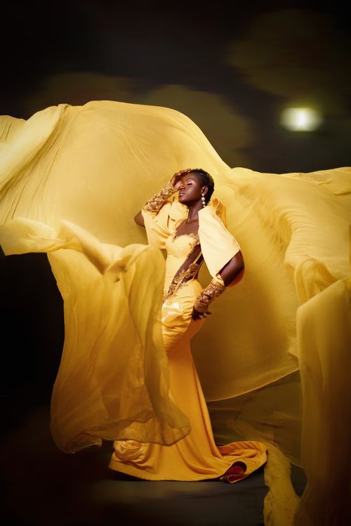 Free A striking photo of a woman in a dramatic yellow dress, highlighted against a soft-lit indoor backdrop. Stock Photo