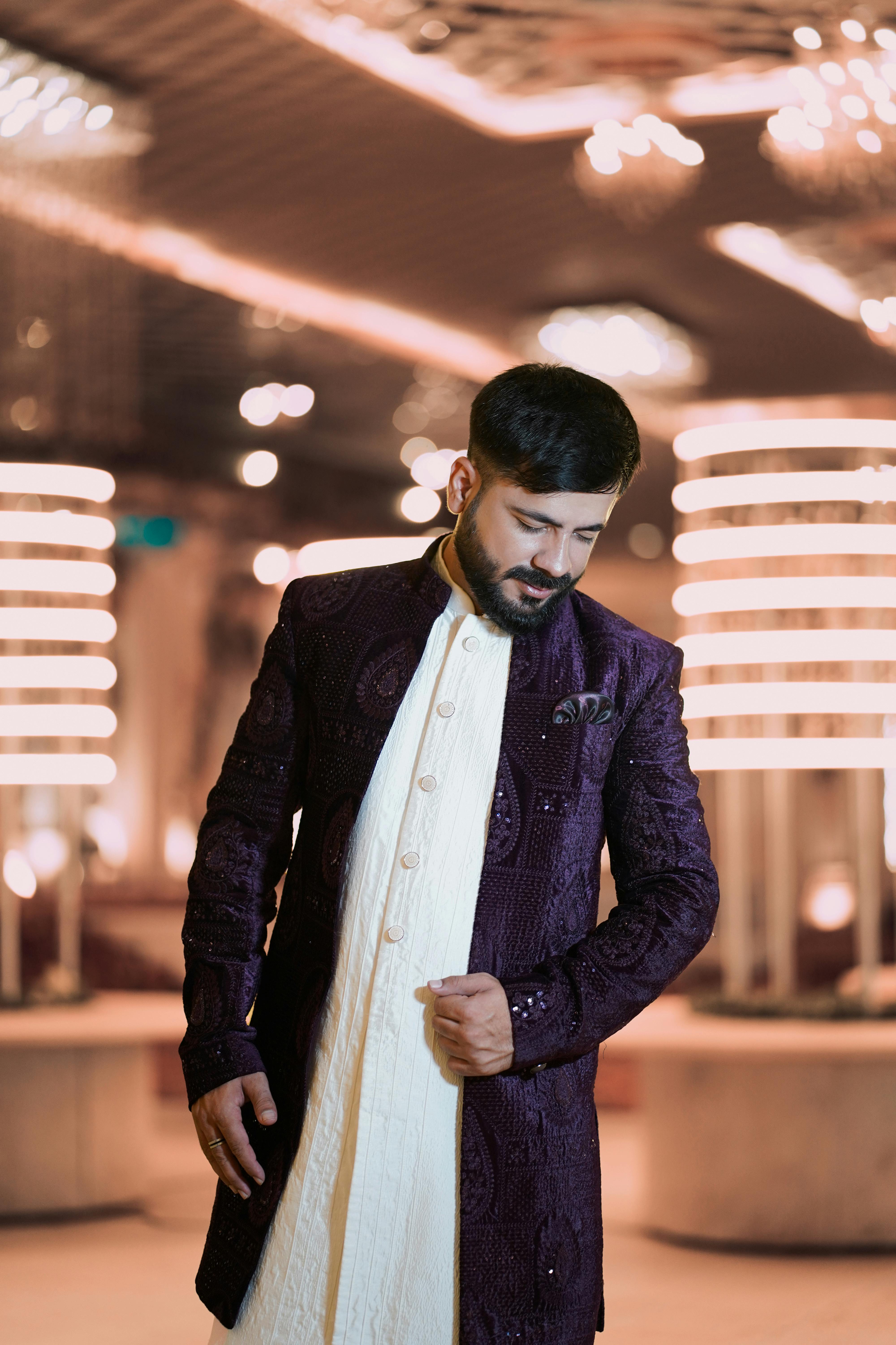 Man wearing traditional Indian attire posing elegantly indoors.