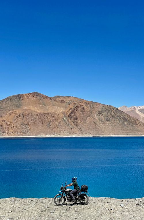 Free A motorcyclist enjoys the breathtaking view of a blue lake with majestic mountains in the background. Stock Photo