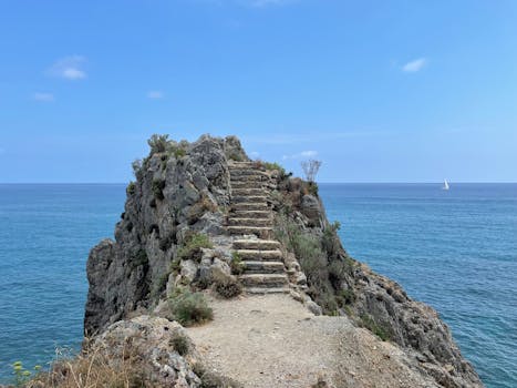 Beautiful rocky cliff with steps overlooking blue sea near Finale Ligure, Italy.
