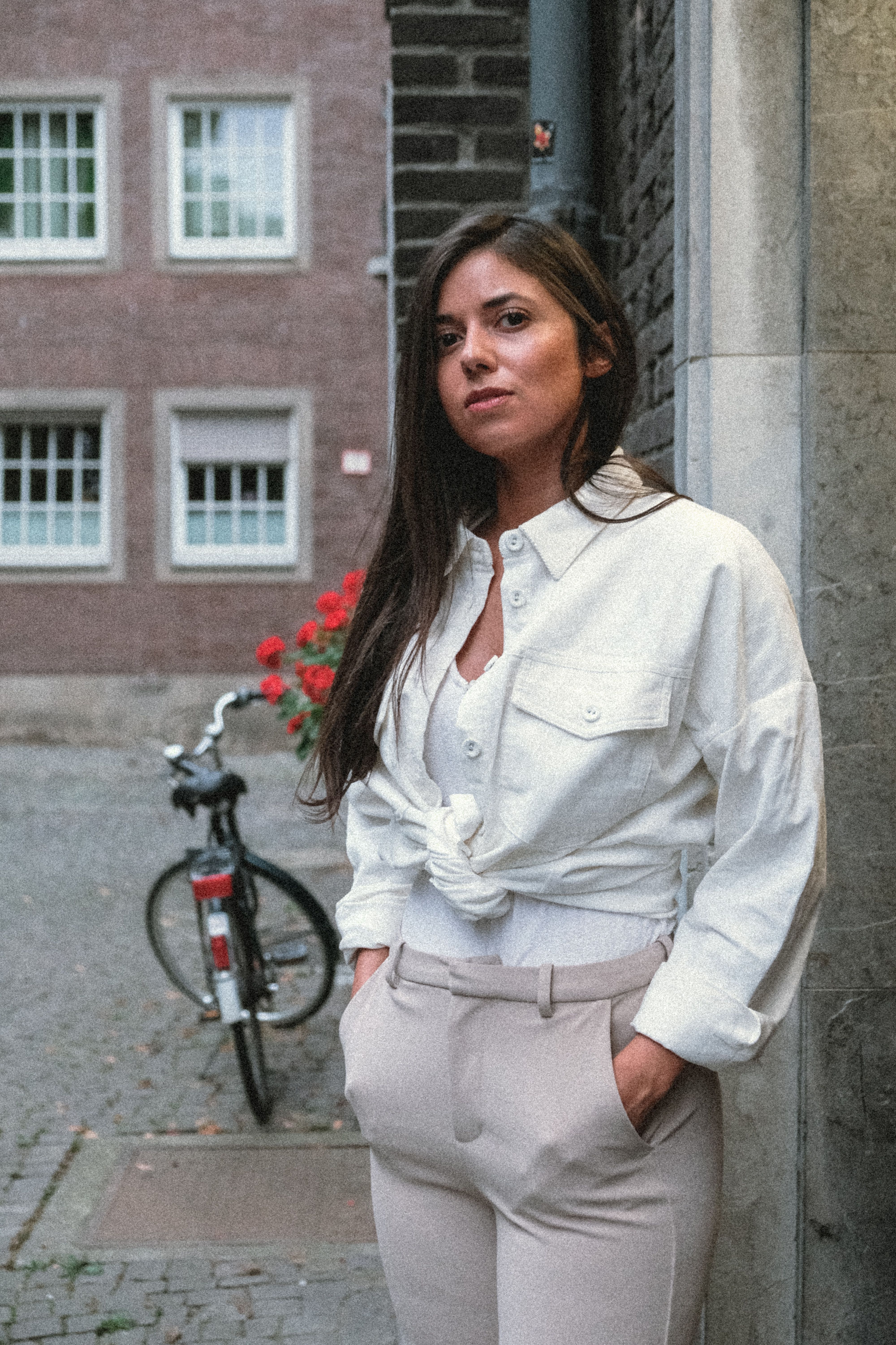 A woman in a white shirt and pants standing by a brick wall · Free ...