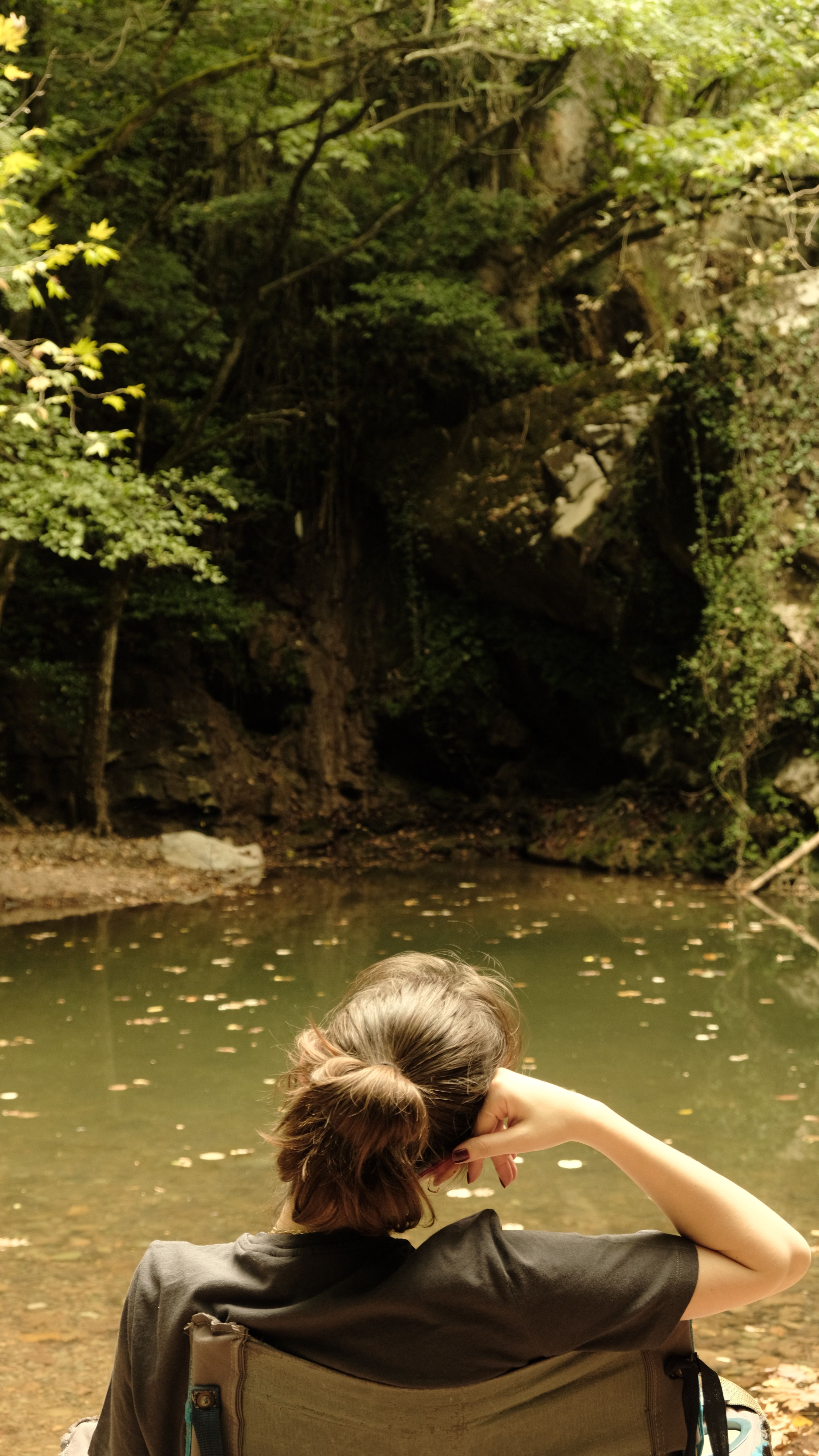 A woman enjoys a peaceful moment by a calm river surrounded by lush forest during summer.