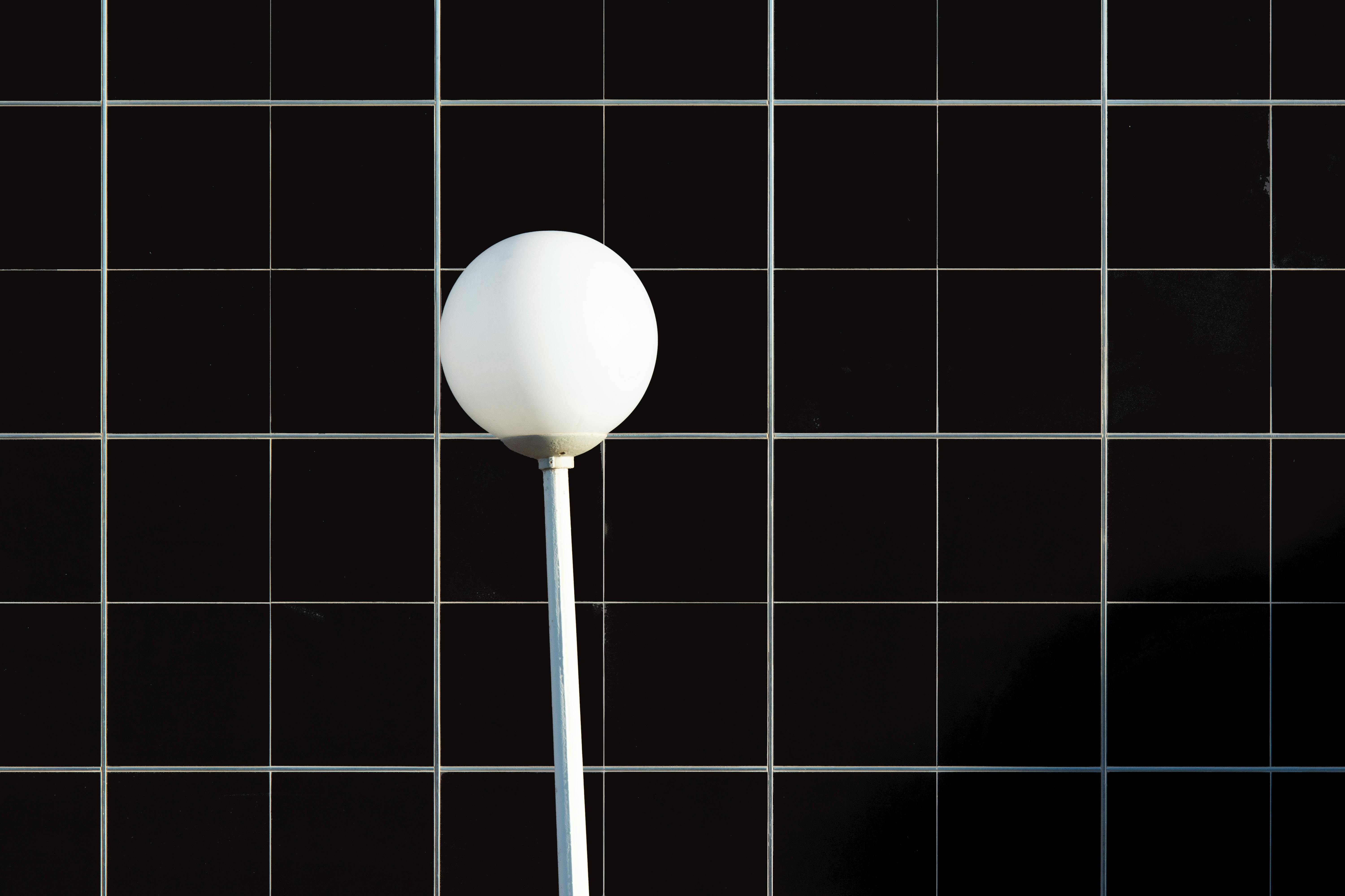 A modern white lamp post contrasting a black tiled wall, creating a geometric visual effect.