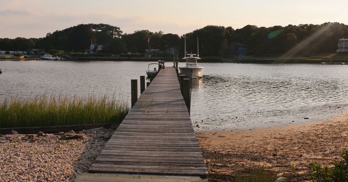 Serene wooden pier at sunset in Hampton Bays, NY, leading to calm waters.