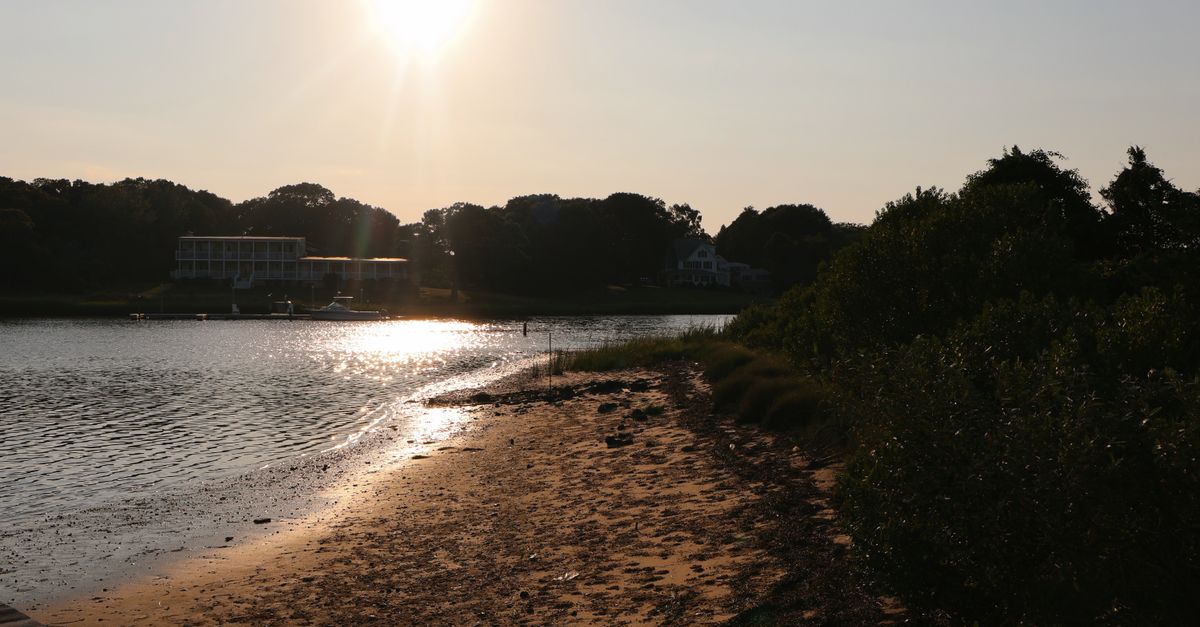 Golden sunset over Hampton Bays beach with serene water reflection.