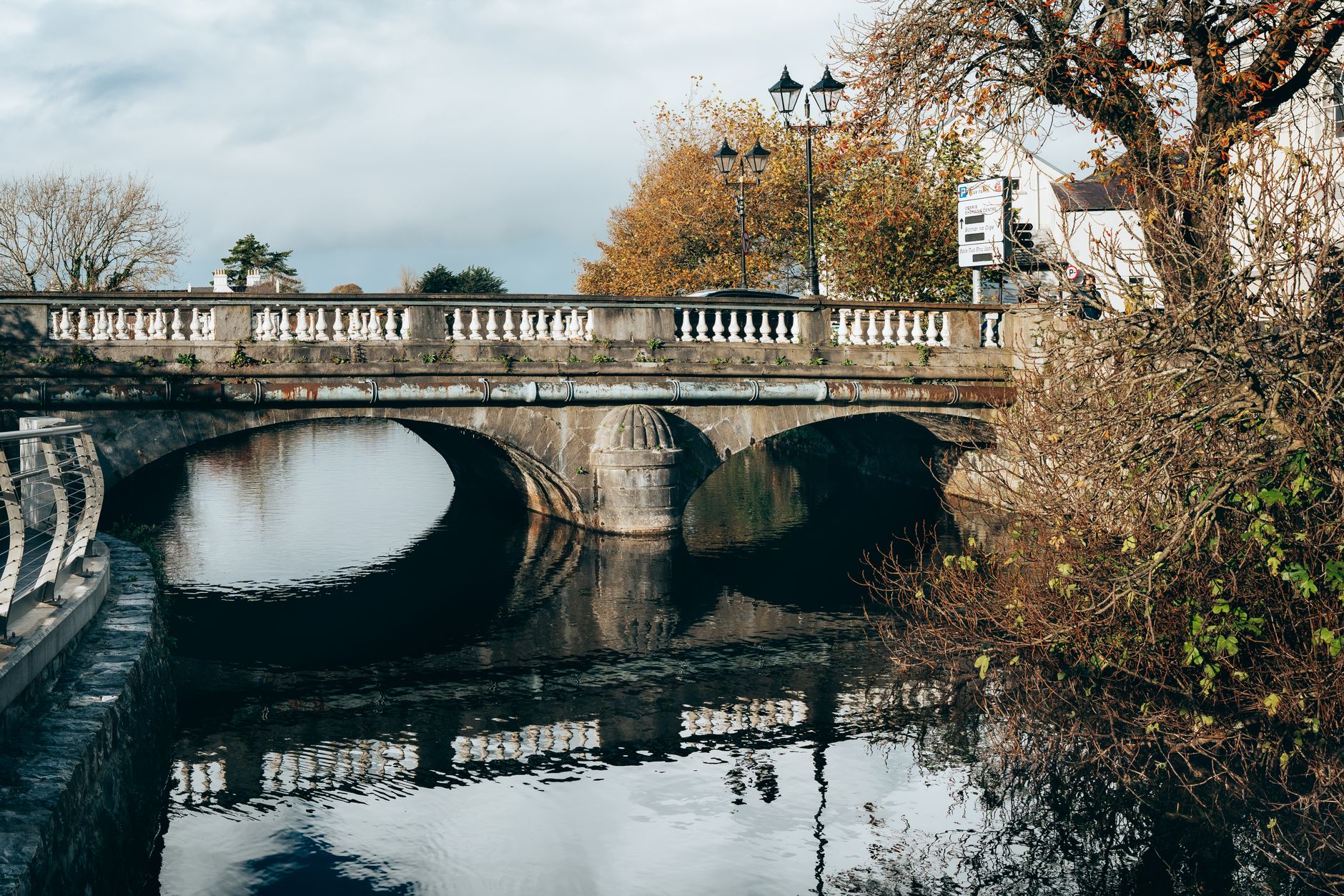 A scenic autumn view of a historic stone bridge over a calm river in Galway, Ireland.