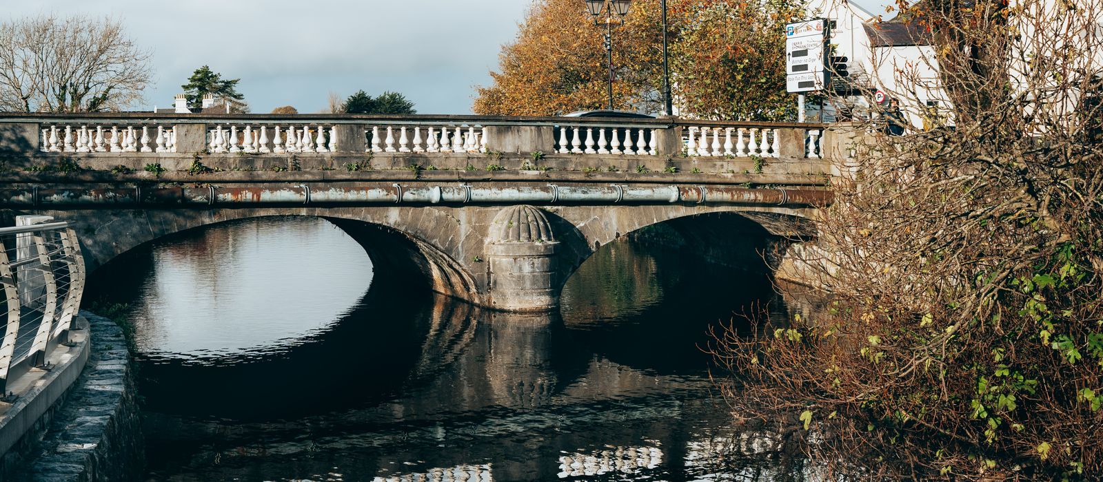 A scenic autumn view of a historic stone bridge over a calm river in Galway, Ireland.