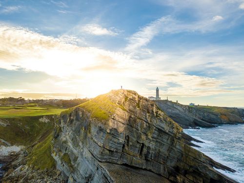 Free Breathtaking view of a lighthouse on a dramatic coastal cliff at sunrise, overlooking the expansive ocean. Stock Photo