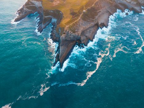 A stunning aerial view of rugged coastal cliffs surrounded by vibrant blue ocean waves.