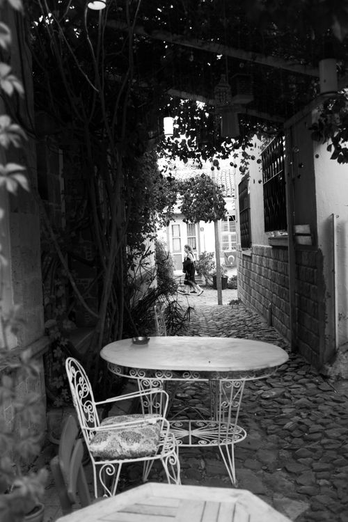 Free An enchanting cobblestone alleyway in Cunda, Türkiye, showing vintage chairs and tables. Stock Photo