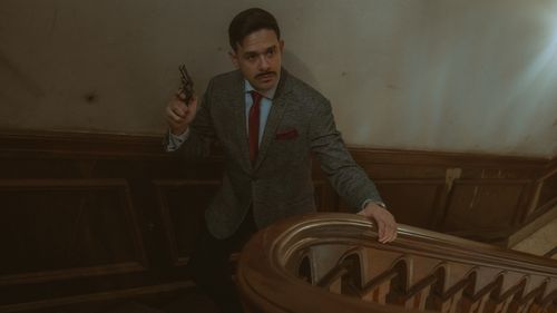 Free Moody scene of a man in a suit with a revolver on an ornate staircase. Stock Photo