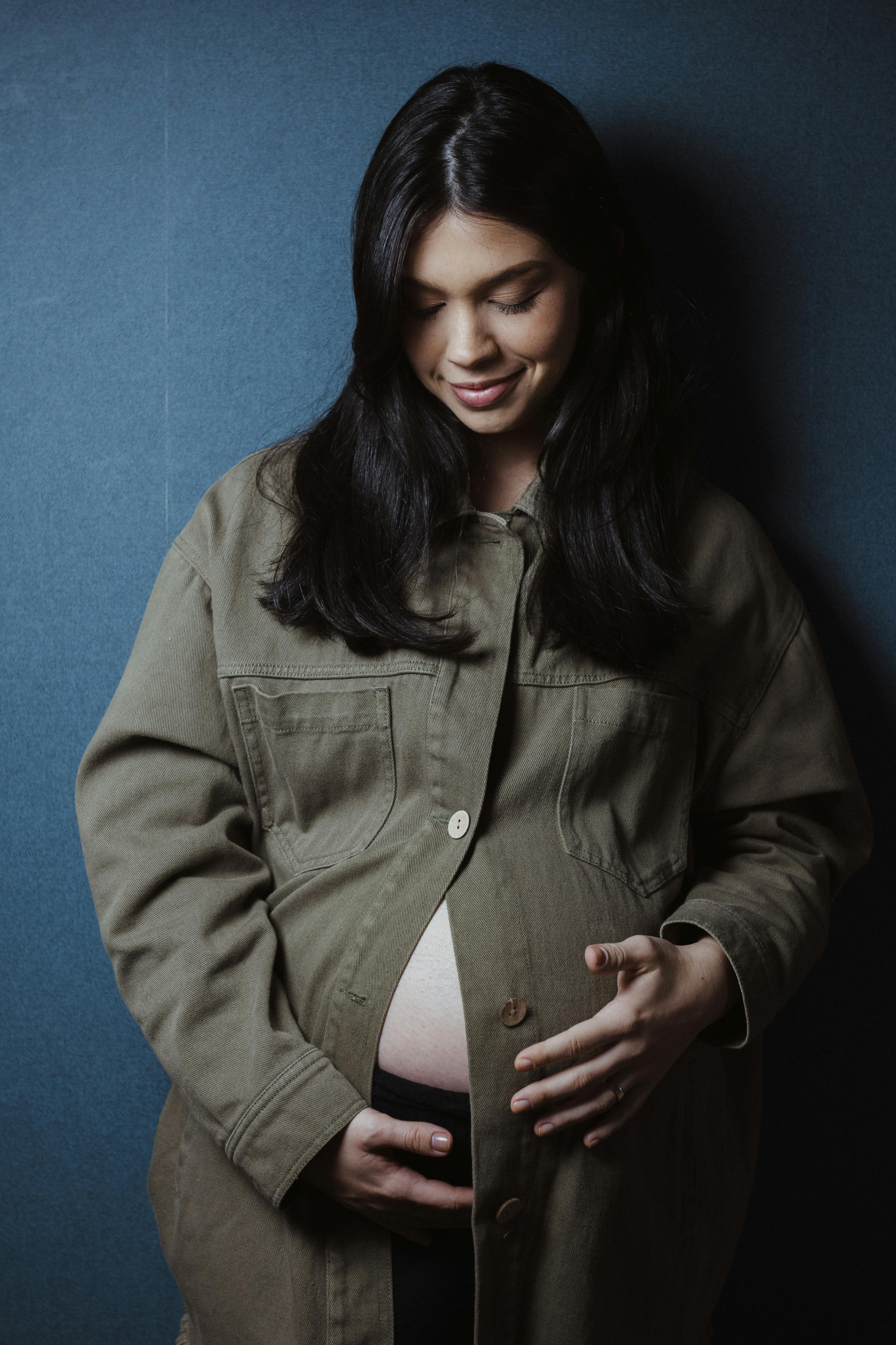 a pregnant woman in a green jacket poses for a portrait